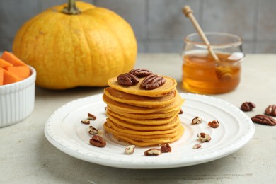 Photo of Tasty pumpkin pancakes with nuts and honey on light grey table, closeup