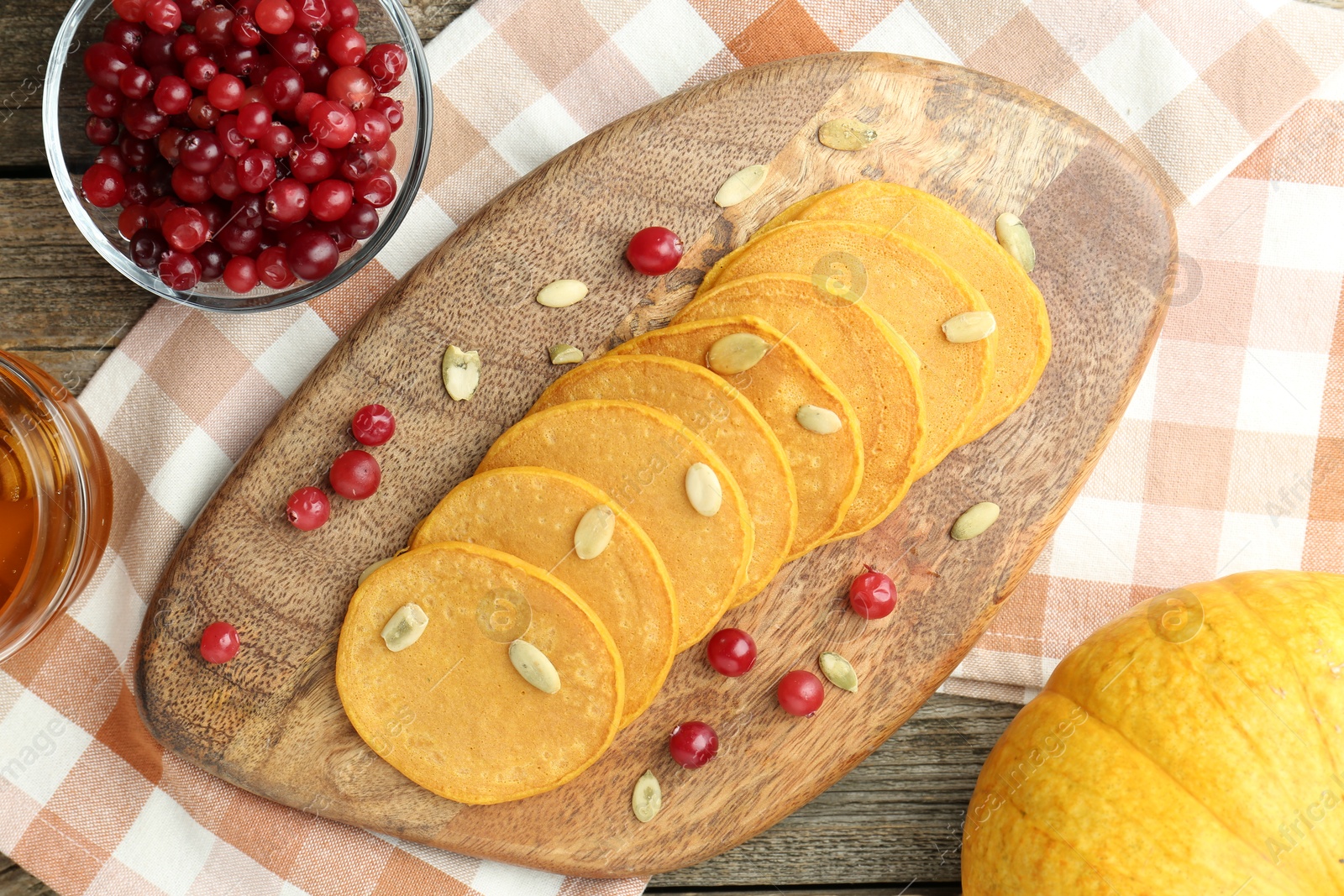 Photo of Tasty pumpkin pancakes with seeds and cranberries on wooden table, top view