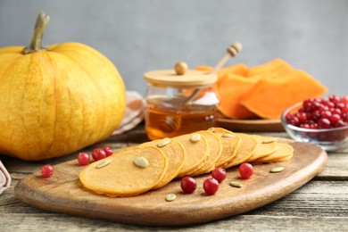 Photo of Tasty pumpkin pancakes with seeds, cranberries and honey on wooden table, closeup