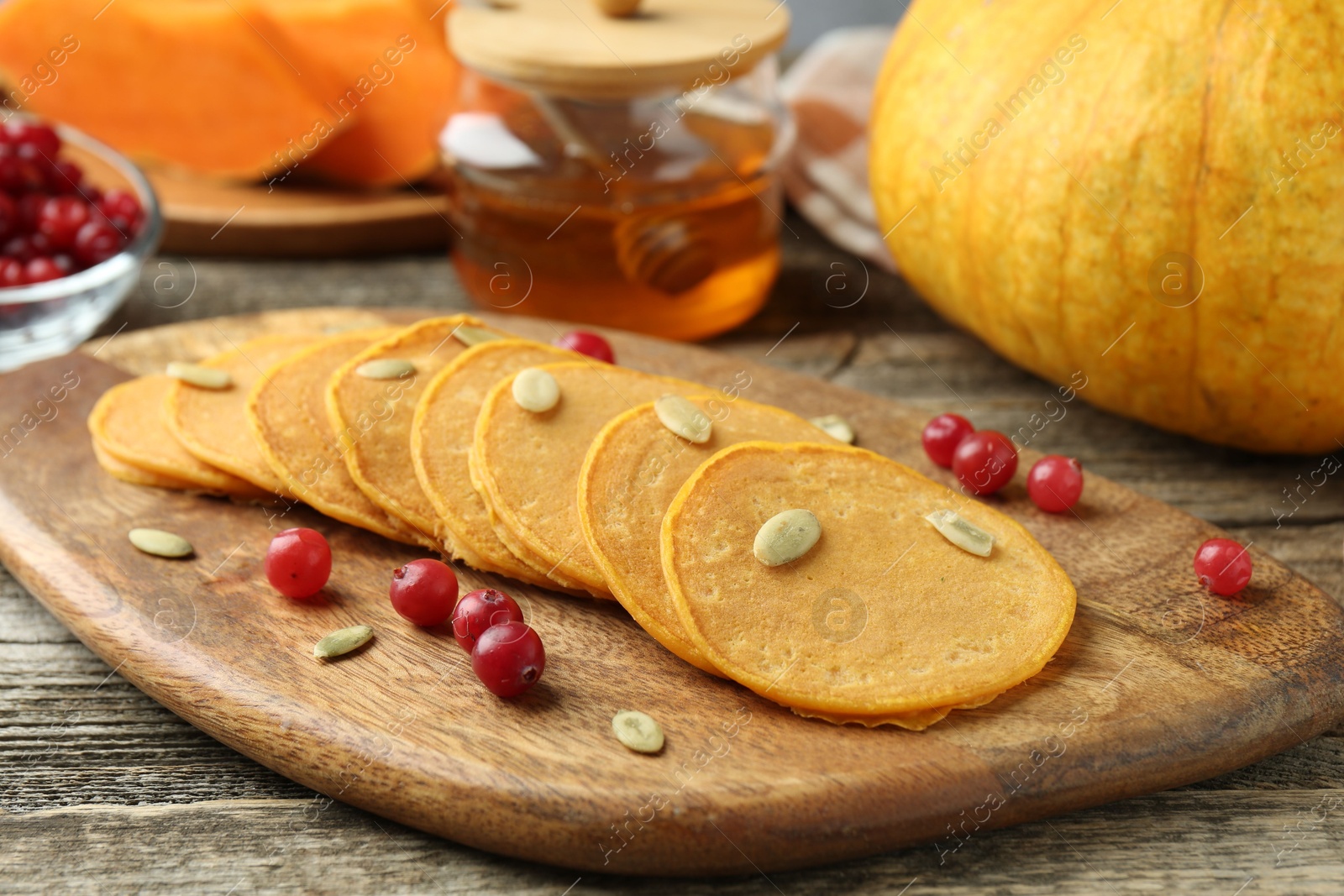 Photo of Tasty pumpkin pancakes with seeds, cranberries and honey on wooden table, closeup