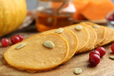 Photo of Tasty pumpkin pancakes with seeds and cranberries on wooden table, closeup