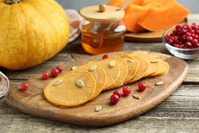 Photo of Tasty pumpkin pancakes with seeds, cranberries and honey on wooden table, closeup