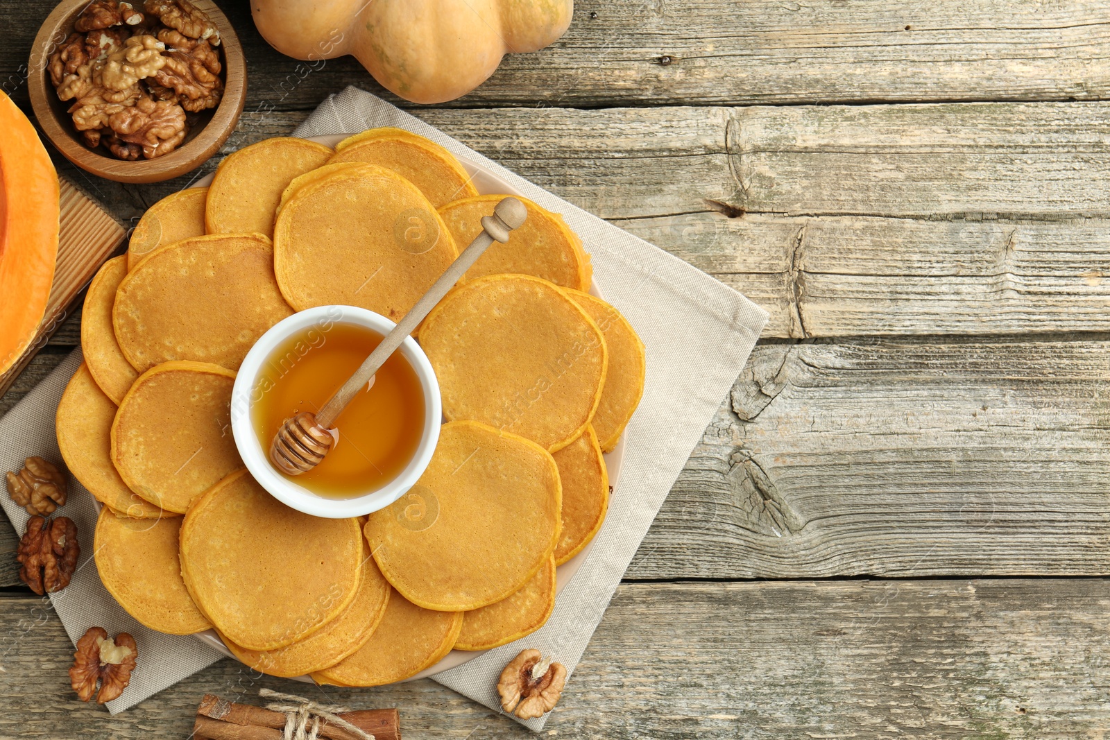 Photo of Tasty pumpkin pancakes, honey, walnuts and cinnamon on wooden table, top view. Space for text