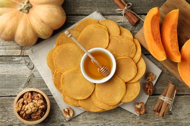 Photo of Tasty pumpkin pancakes, honey, walnuts and cinnamon on wooden table, flat lay