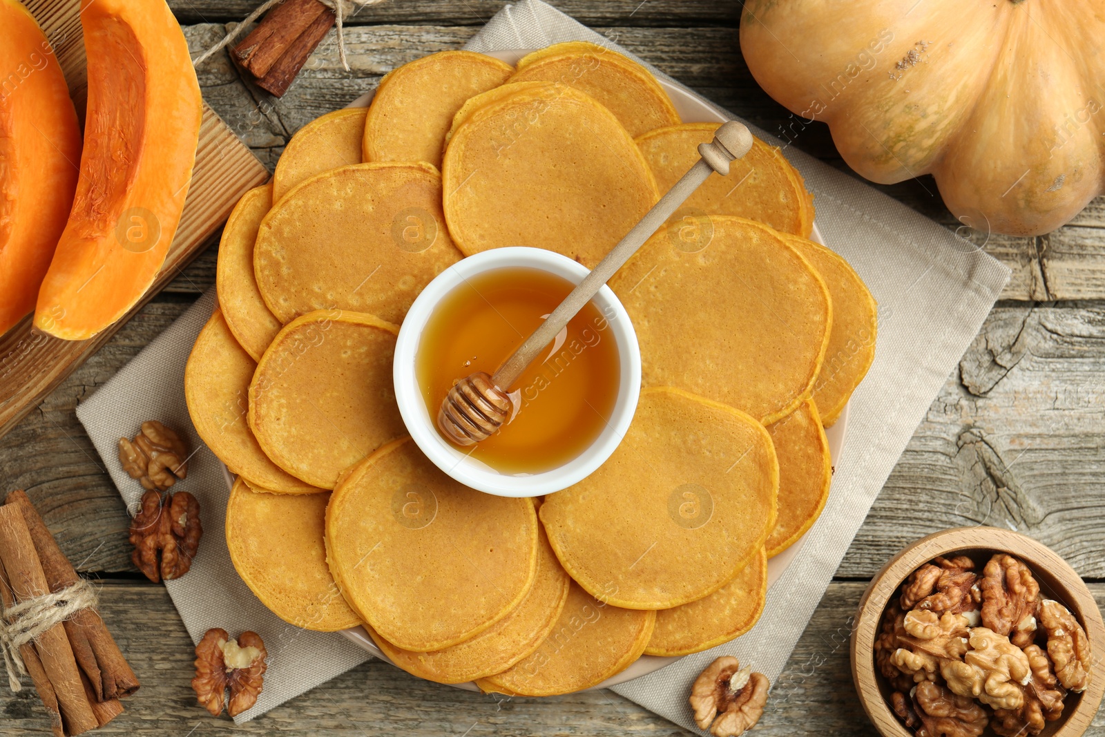 Photo of Tasty pumpkin pancakes, honey, walnuts and cinnamon on wooden table, flat lay