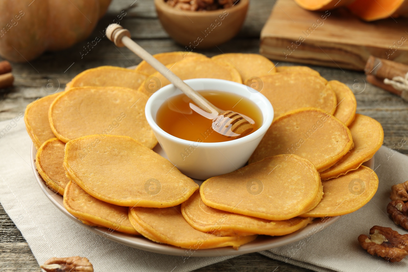 Photo of Tasty pumpkin pancakes, honey and walnuts on wooden table, closeup