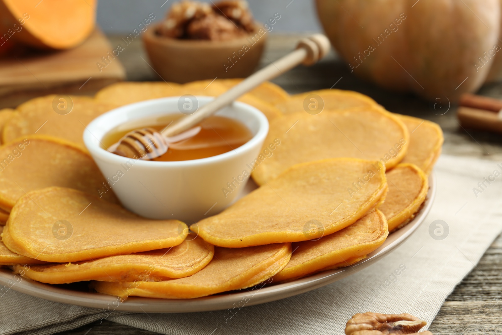 Photo of Tasty pumpkin pancakes and honey on table, closeup