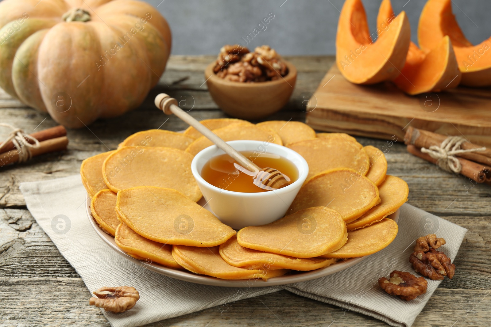 Photo of Tasty pumpkin pancakes, honey and walnuts on wooden table, closeup