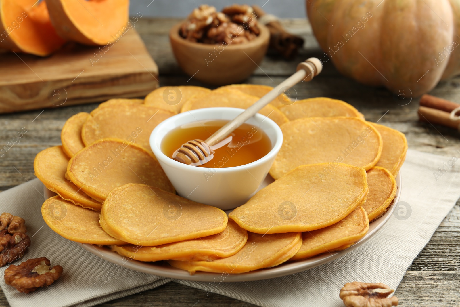 Photo of Tasty pumpkin pancakes, honey and walnuts on wooden table, closeup