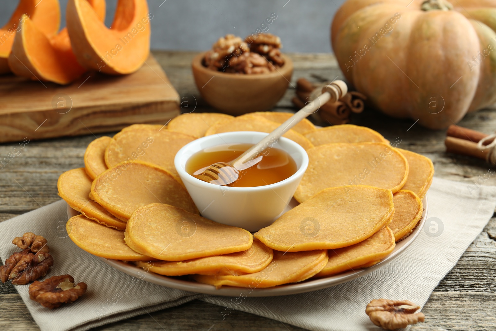 Photo of Tasty pumpkin pancakes, honey and walnuts on wooden table, closeup