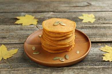 Photo of Tasty pumpkin pancakes with seeds and maple leaves on wooden table, closeup