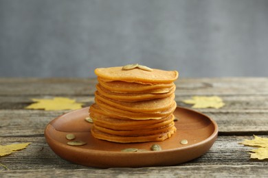 Photo of Tasty pumpkin pancakes with seeds and maple leaves on wooden table, closeup