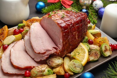 Tasty baked ham served with vegetables and oranges on black wooden table, closeup