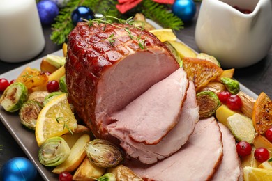 Photo of Tasty baked ham served with vegetables and oranges on black wooden table, closeup