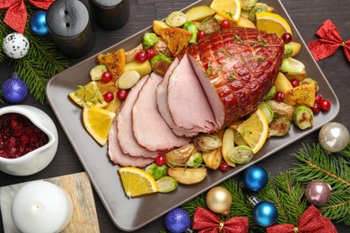 Photo of Tasty baked ham served with vegetables and oranges on black wooden table, flat lay