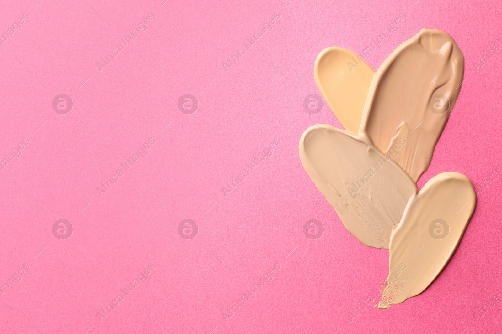 Photo of Foundation on pink background, top view with space for text. Smears of cosmetic product