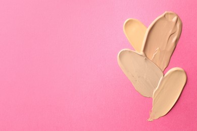 Photo of Foundation on pink background, top view with space for text. Smears of cosmetic product