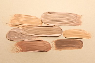 Photo of Samples of different foundations on beige background, top view