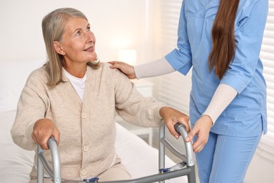 Photo of Nurse helping senior woman with walking frame in clinic