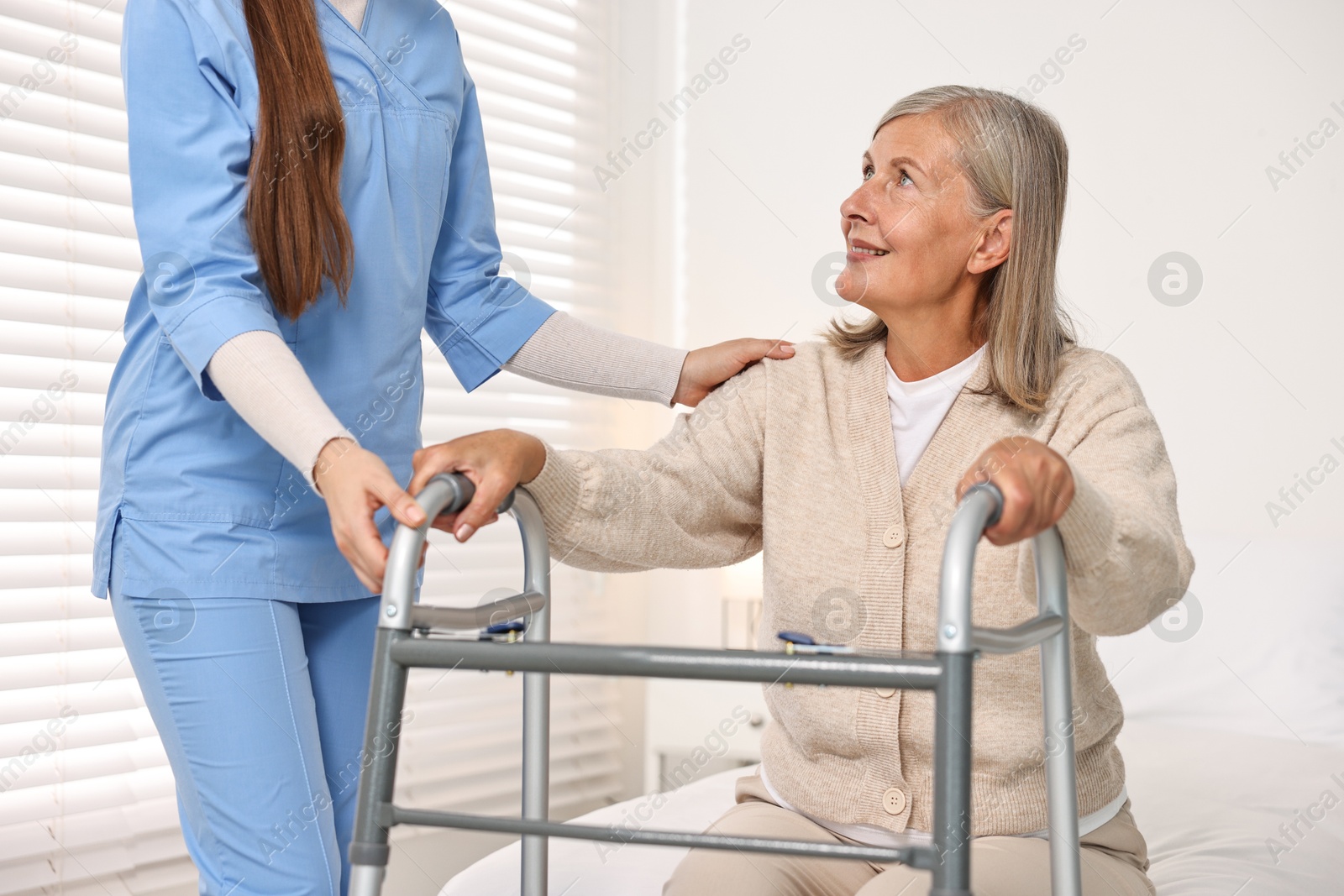 Photo of Nurse helping senior woman with walking frame in clinic