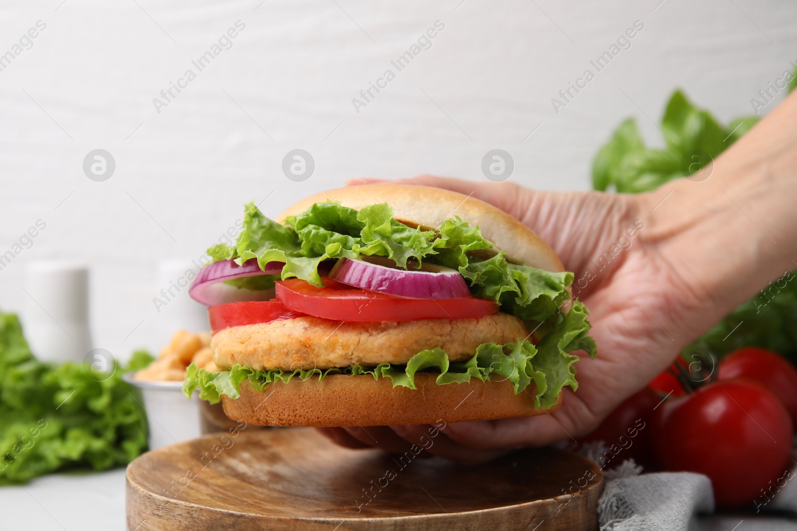 Photo of Woman holding vegetarian burger with chickpea cutlet at table, closeup