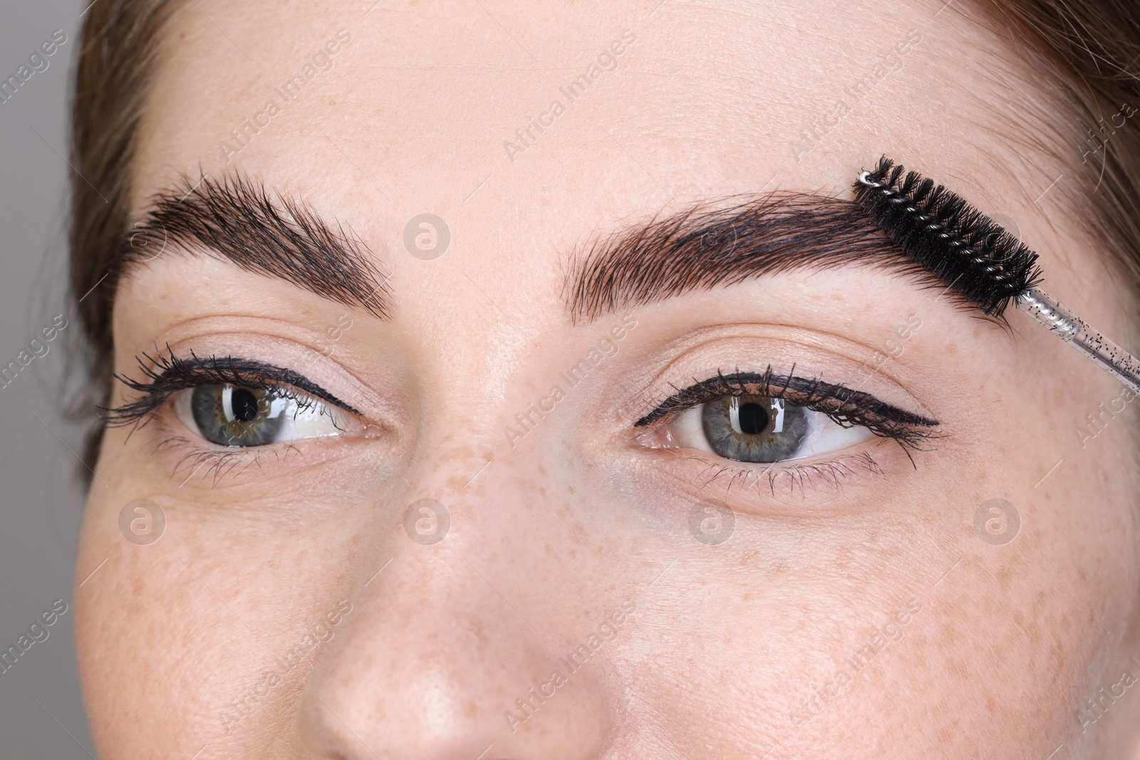 Photo of Brow lamination. Woman combing eyebrows with brush, closeup