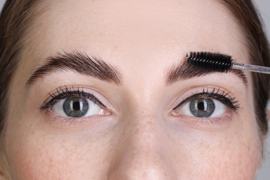 Photo of Brow lamination. Woman combing eyebrows with brush, closeup