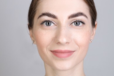 Woman after brow lamination procedure on grey background, closeup