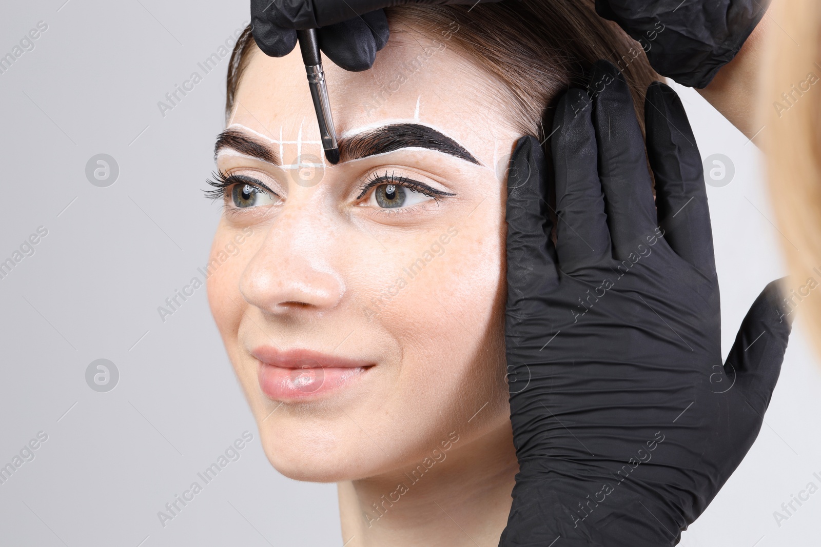 Photo of Young woman undergoing henna eyebrows dyeing on light background, closeup