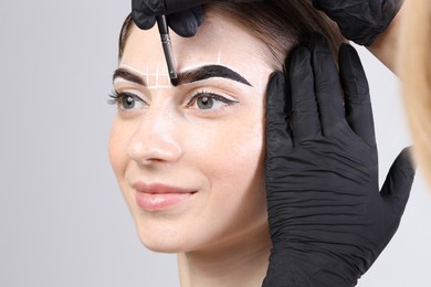 Photo of Young woman undergoing henna eyebrows dyeing on light background, closeup