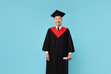 Happy student with diploma after graduation on light blue background