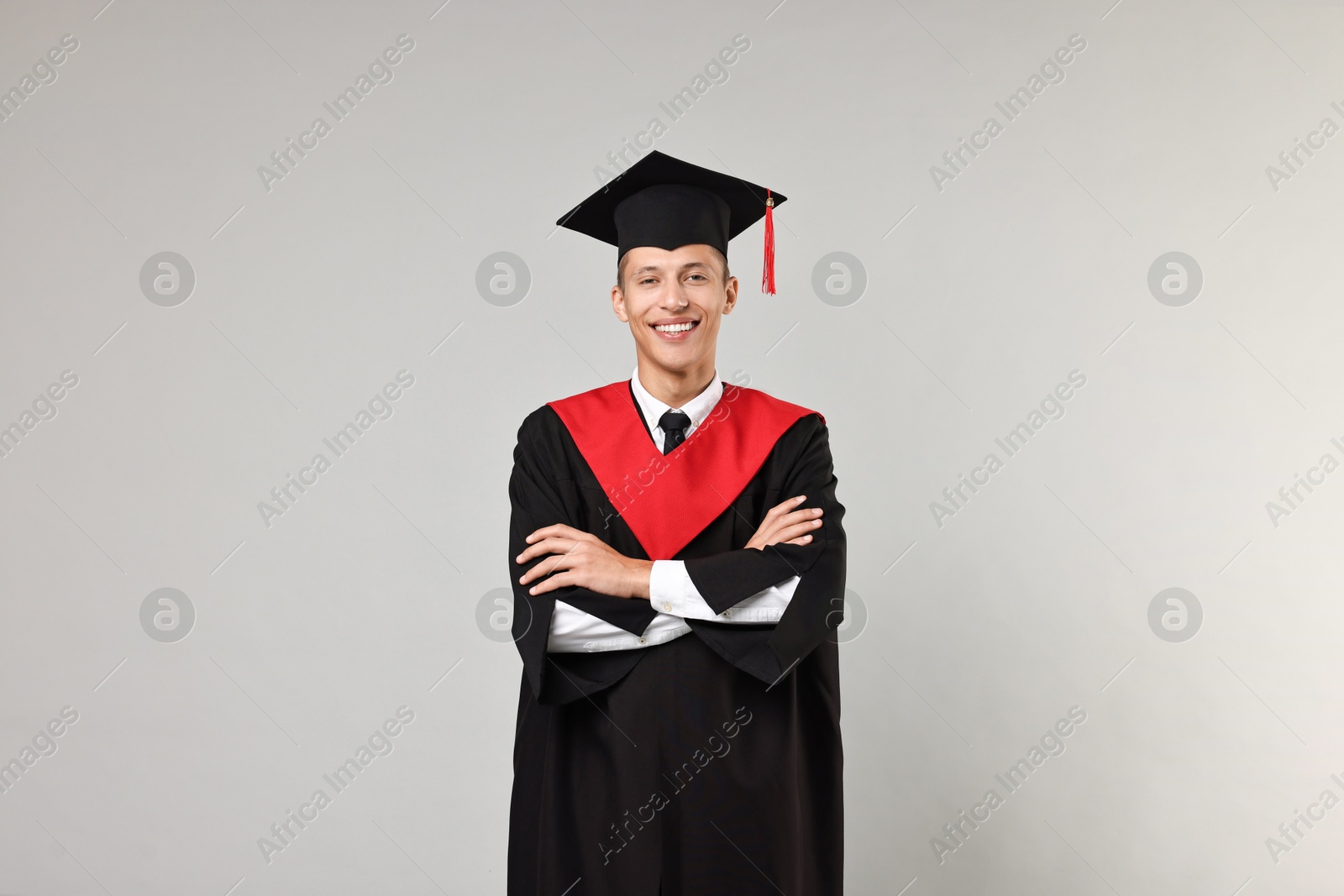 Photo of Happy student with crossed arms after graduation on grey background