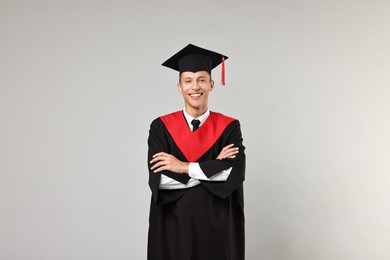 Photo of Happy student with crossed arms after graduation on grey background