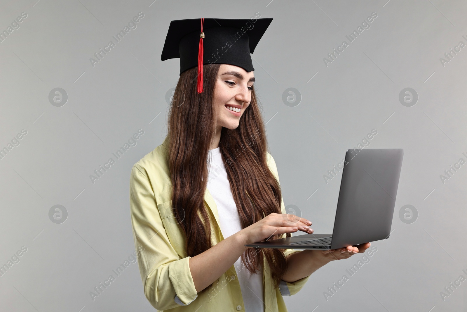 Photo of Happy student with laptop after graduation on grey background