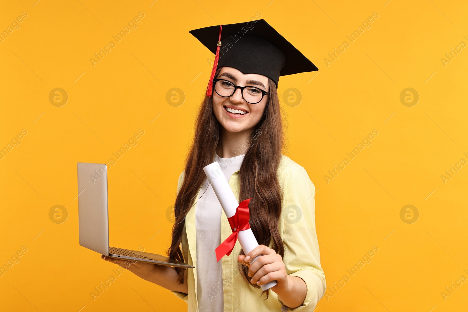 Photo of Happy student with laptop and diploma after graduation on orange background