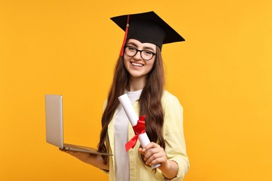 Happy student with laptop and diploma after graduation on orange background