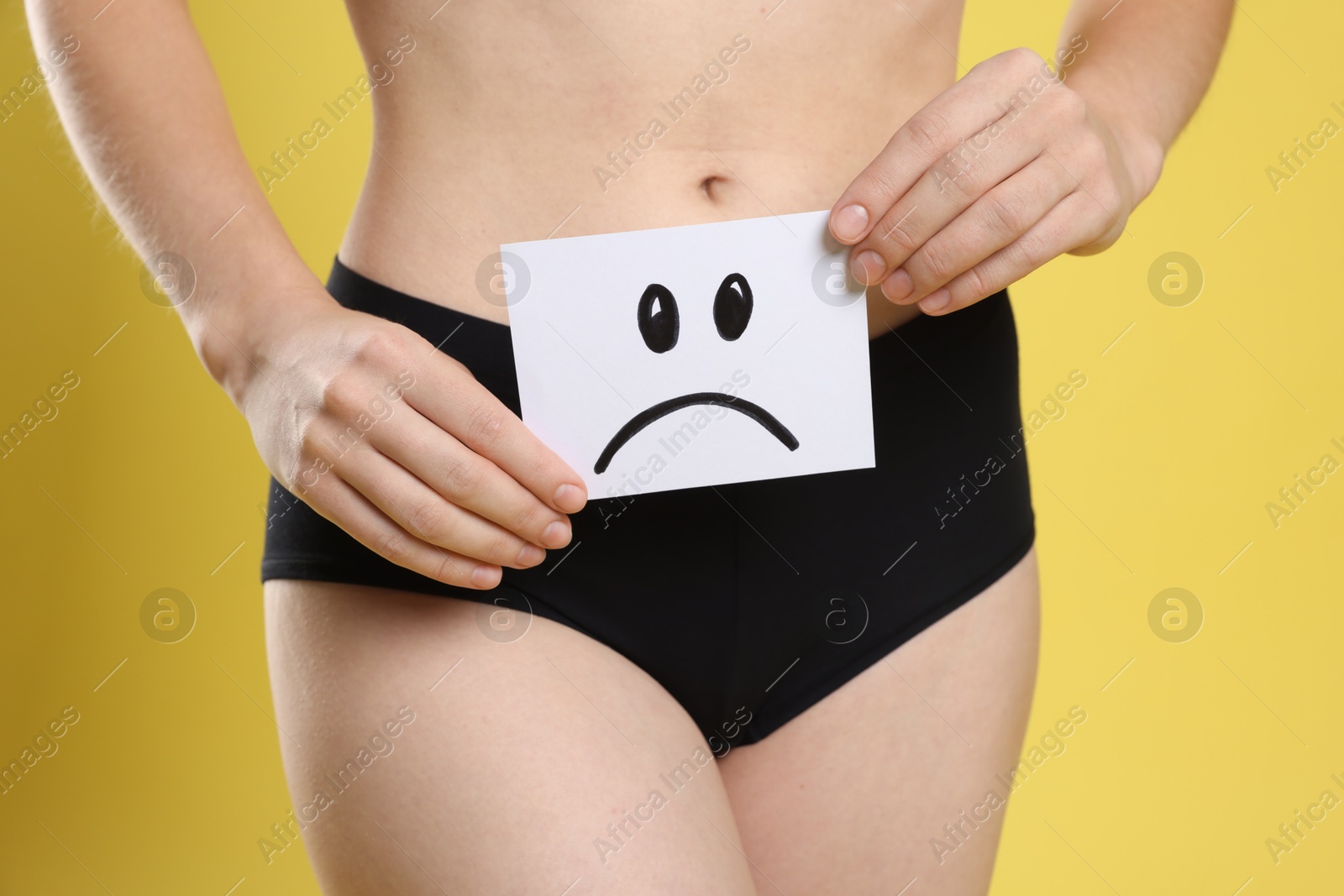 Photo of STD (sexually transmitted disease). Woman holding sticky note with drawn sad face on yellow background, closeup