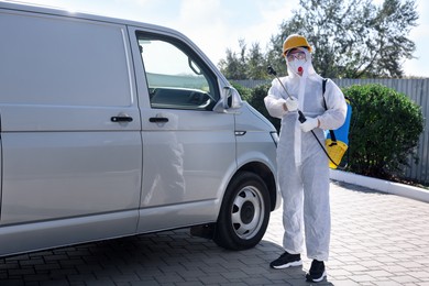 Photo of Pest control worker with spray tank near gray minibus outdoors