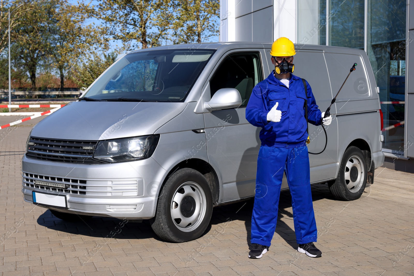 Photo of Pest control worker with spray tank showing thumbs up outdoors