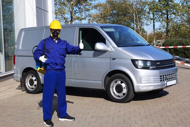 Photo of Pest control worker with spray tank showing thumbs up outdoors