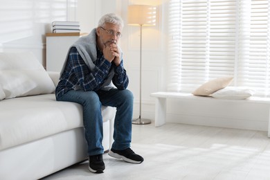 Photo of Lonely senior man sitting on sofa at home. Space for text