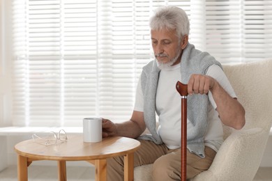 Photo of Lonely senior man with walking cane and cup of drink sitting at table indoors