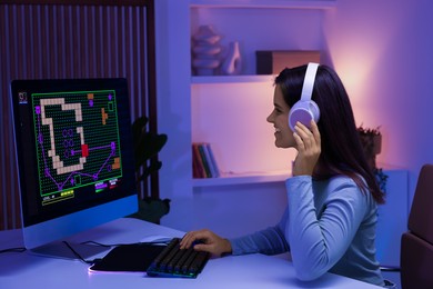 Smiling woman in headphones playing video game with keyboard at table indoors