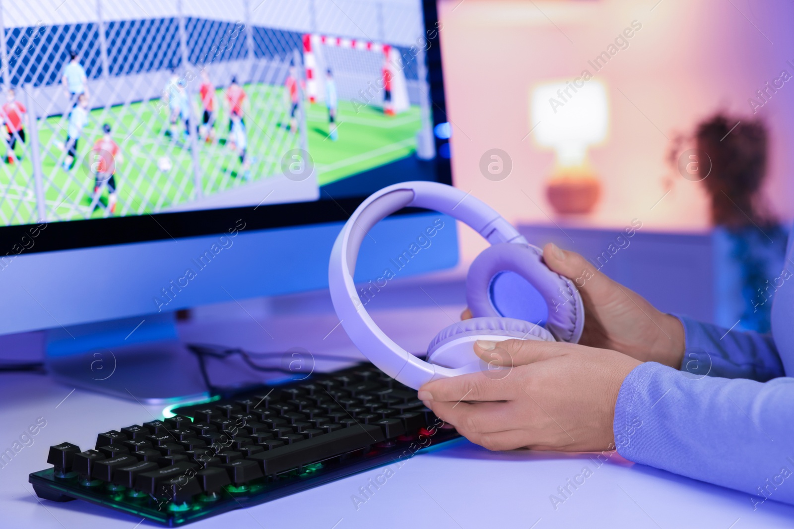 Photo of Woman with headphones, computer keyboard and monitor on white table indoors, closeup