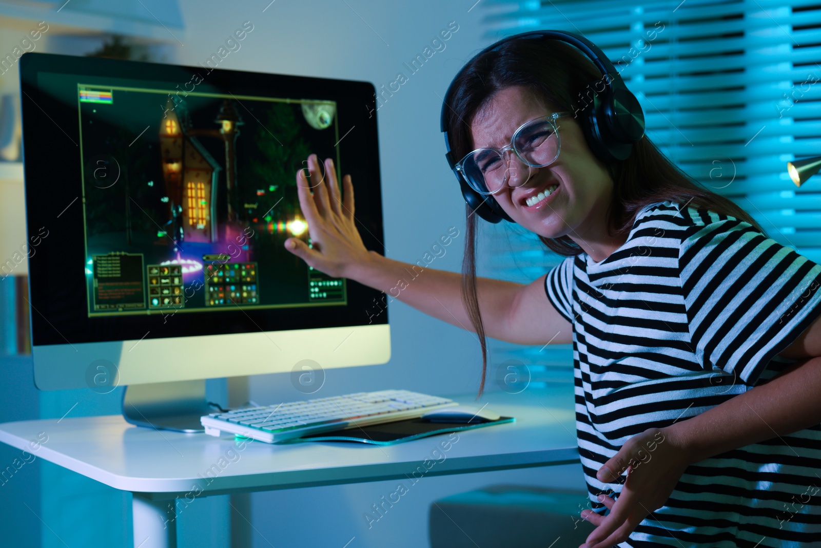 Photo of Frustrated woman playing video game with keyboard at table indoors