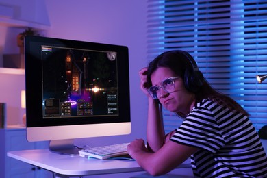 Frustrated woman playing video game with keyboard at table indoors