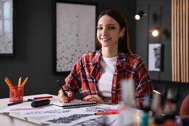 Photo of Smiling tattoo artist drawing sketch with pen at white table in salon