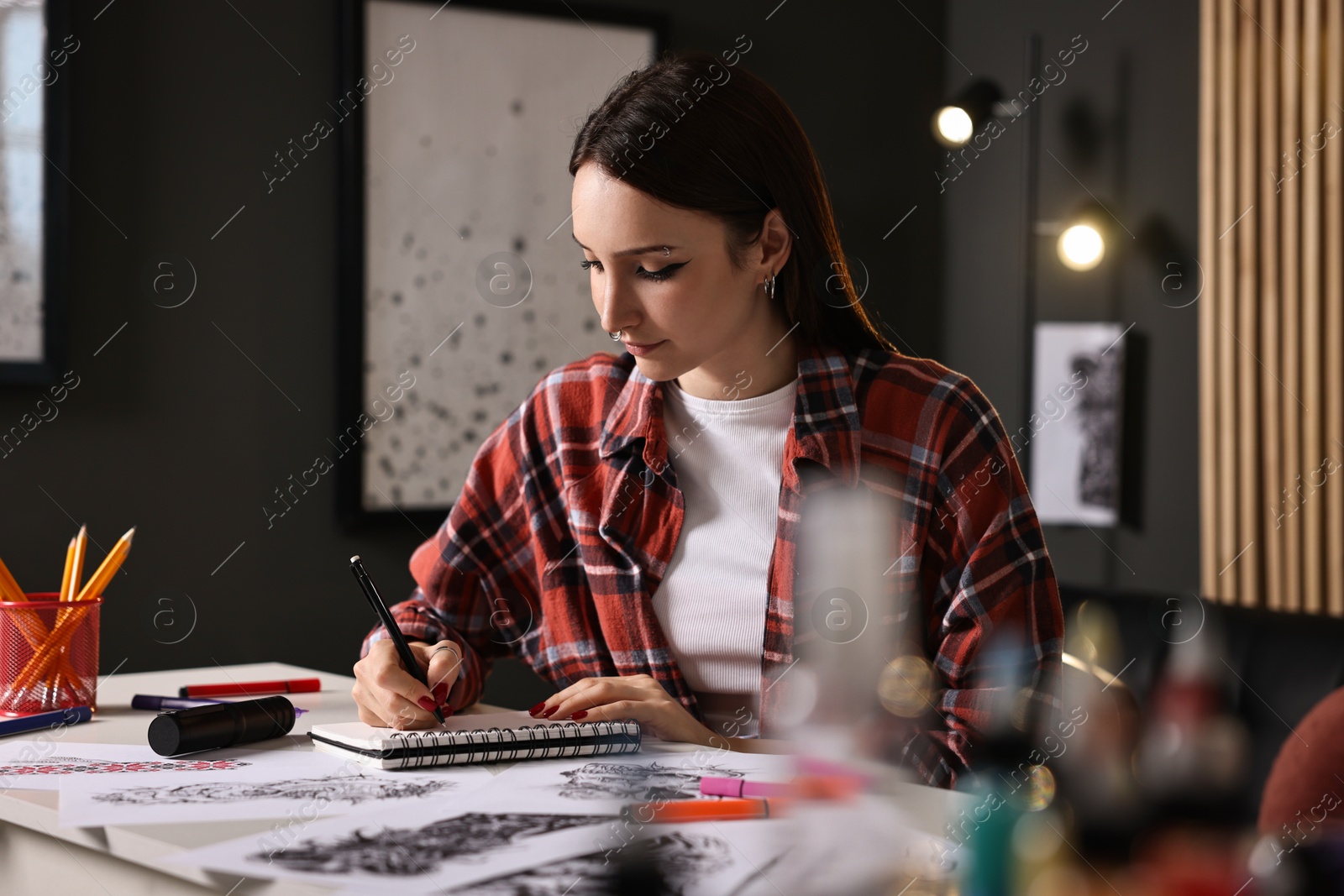 Photo of Tattoo artist drawing sketch with pen at white table in salon