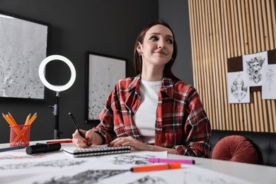 Photo of Tattoo artist drawing sketch with pen at white table in salon, low angle view