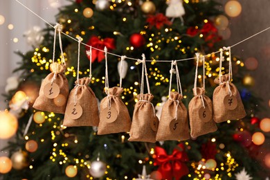 Photo of Advent calendar with gifts hanging near Christmas tree indoors